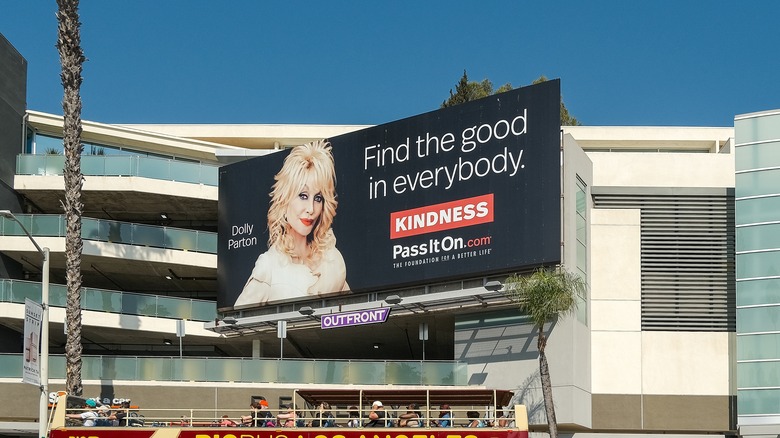 A billboard featuring Dolly Parton saying "find the good in everybody" above a busy LA street