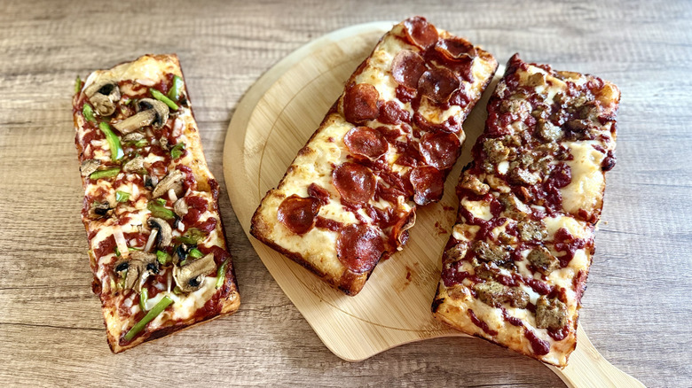 Three Domino Detroit-style rectangular pizzas with different toppings