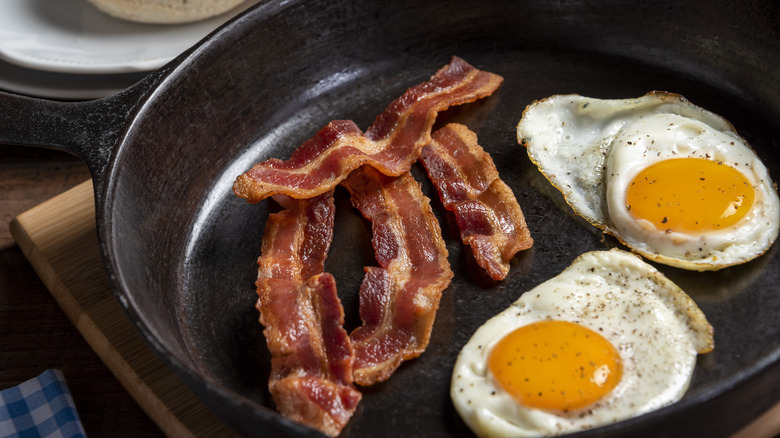 3 pieces of cooked bacon next to two over easy eggs on a cast iron pan