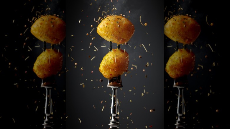 A fork puncturing two potatoes on a black background