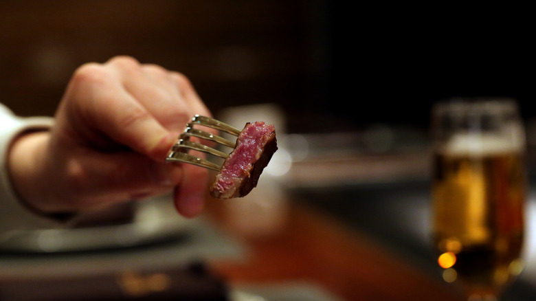 A diner holds a bite of Kobe beef on a fork