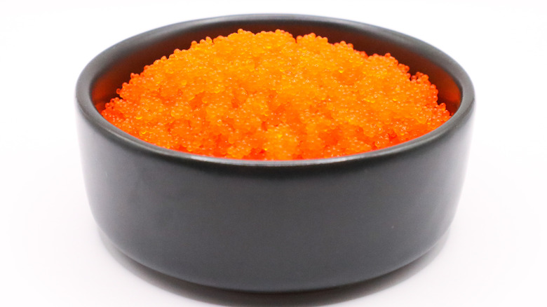 A small black bowl filled with bright orange shrimp roe with a white background.