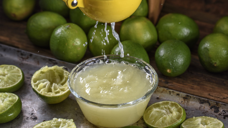 Lime juice is squeezed into a glass bowl surrounded by limes