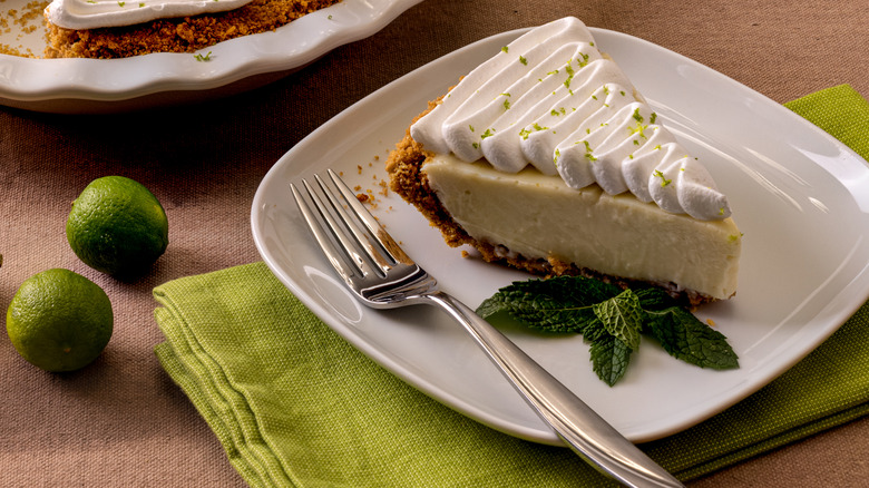 Key lime pie on a plate with a fork next to limes
