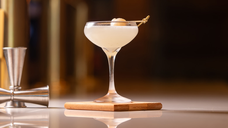 A cocktail on a wooden coaster with two steel jiggers