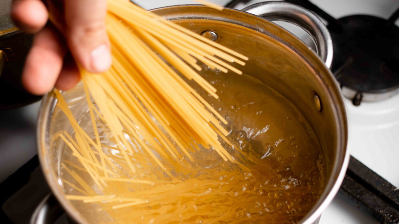A person adds a handful of spaghetti noodles to a pot of boiling water