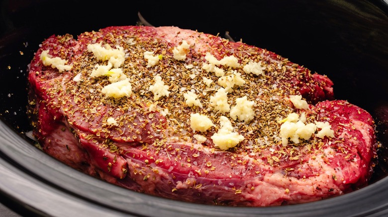 Beef in slow cooker with garlic and seasonings on top