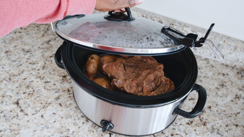 Person lifting lid off slow cooker with beef inside