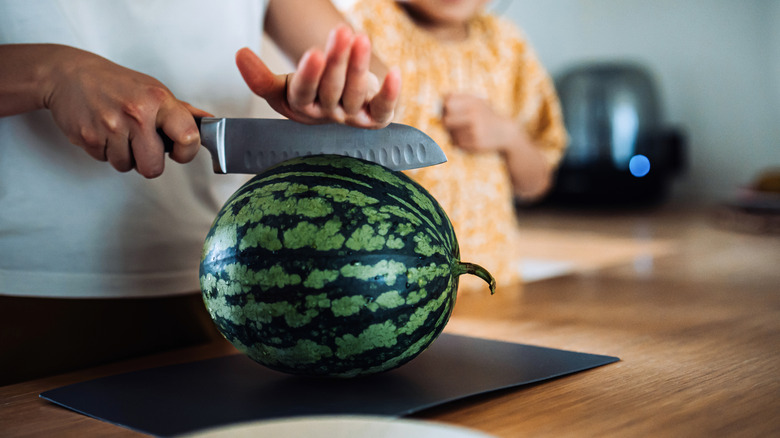 A man holds a knife to cut a watermelon on a cutting board