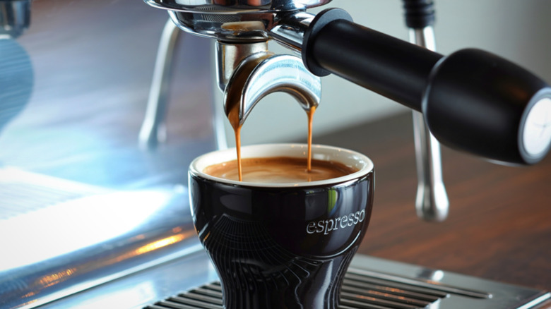 Espresso getting brewed into a black and white ceramic cup