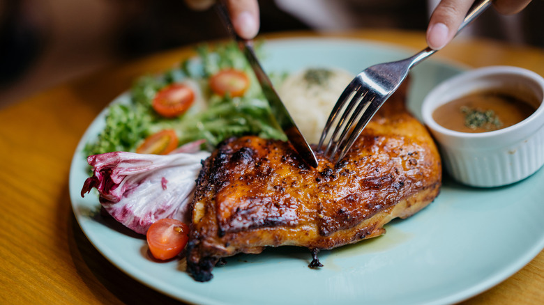 For and knife cutting into chicken leg quarter