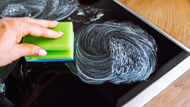 woman's hand washes glass surface an electric stove or induction stove with detergent, wipes traces food preparation from glass with a sponge.