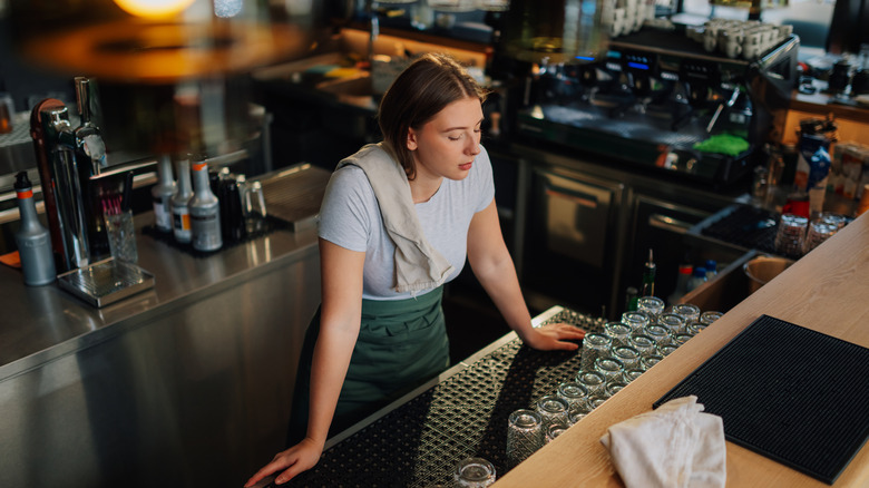 A bartender standing behind the bar looking tired.