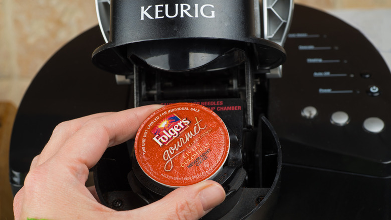 Hand placing a Folgers K-Cup in a Keurig coffee machine