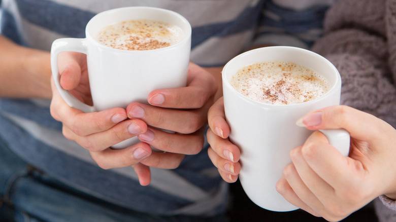 Hands holding white mugs of hot cocoa