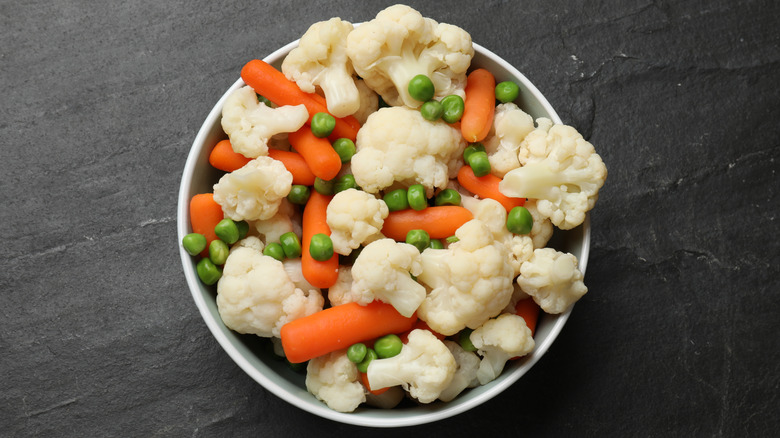 A bowl of steamed carrots, cauliflower, and peas