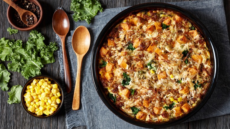 Breakfast casserole with corn and cheese in baking dish on dark wooden table with wooden spoons