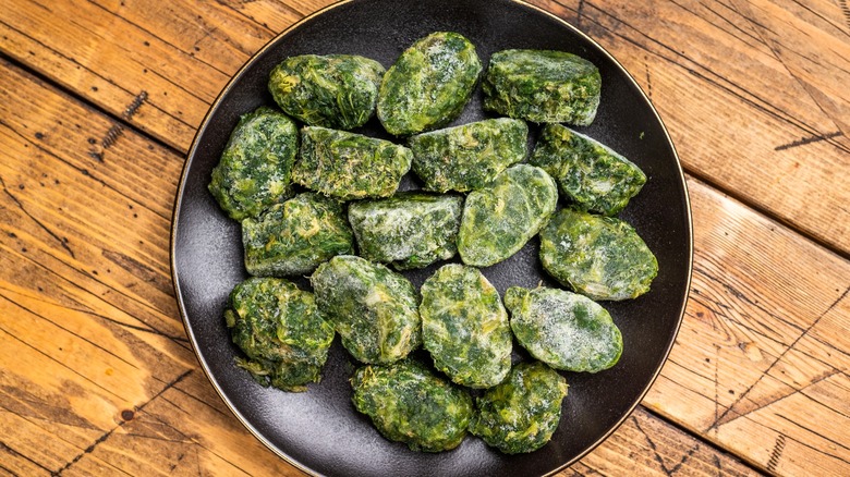 Frozen blocks of spinach in dark bowl