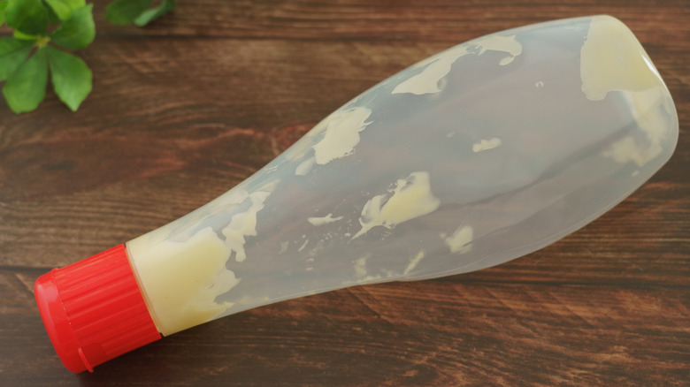 A mostly empty squeeze bottle of mayonnaise laying flat on its side