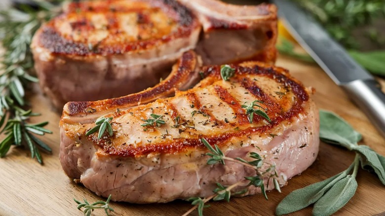 Seared bone-in pork chops with rosemary, thyme, and sage on wood board