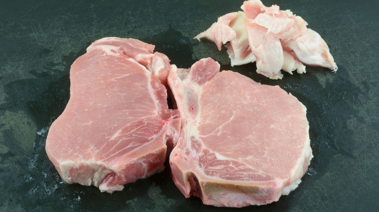 Two raw pork chops with excess fat cut off on the side