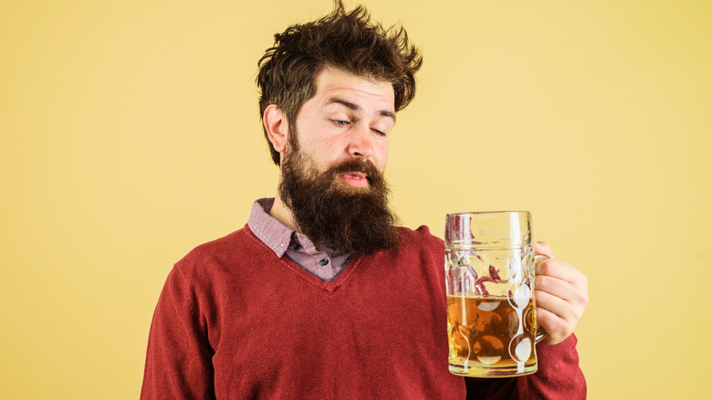 bearded man regarding a mug of beer with a dubious expression