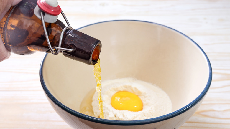 bottle of beer being poured into a bowl with a raw egg and flour