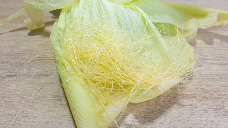 Raw corn silk sitting on a green corn husk