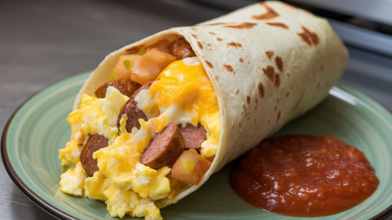 A breakfast burrito with sliced hot dog, cheese, and scrambled egg