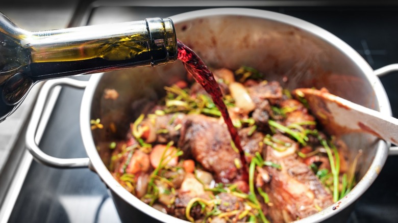 Wine being poured into large pot with meat.