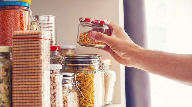 Hand placing jar of corn on pantry shelf