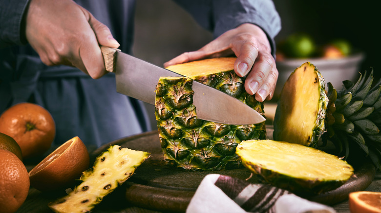 hands using knife to peel a pineapple