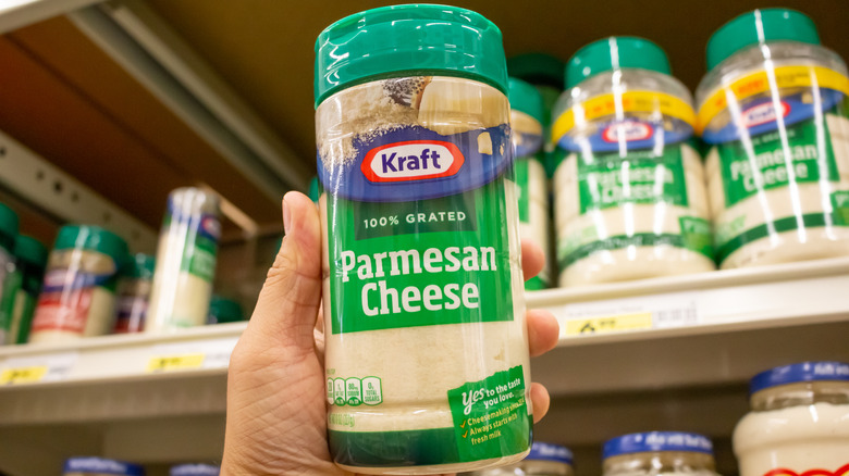 A person in a grocery store holding up a bottle of Kraft parmesan cheese