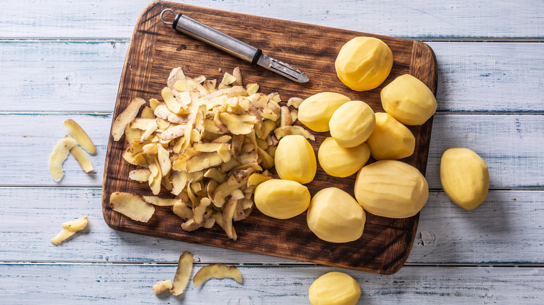Peeled potatoes beside a peeler and potato skin on a cutting board