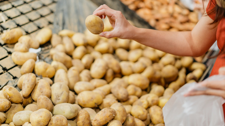 A person picking potatoes out of a bin at the grocery store
