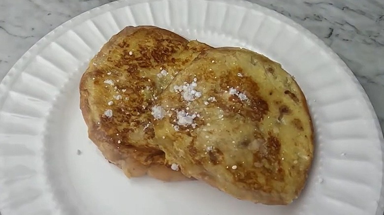 Two pieces of bagel French toast on a paper plate, with icing sugar sprinkled on the top