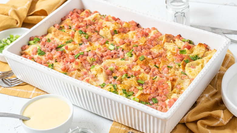 Breakfast casserole with eggs, cheese, diced ham, and green onions in a rectangular white pan