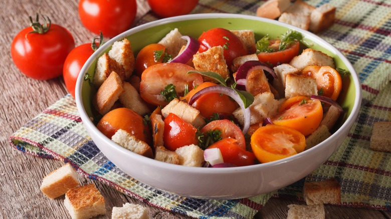 bowl of Tuscan-style panzanella salad made with bread, tomatoes, and red onions sitting on a checked cloth