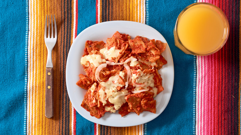 Top view of chilaquiles in red salsa and glass of orange juice on sarape blanket