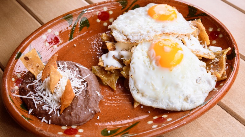 Plate with eggs over chilaquiles and beans on the side