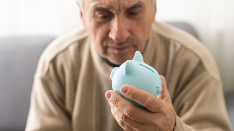 older man frowning at piggy bank