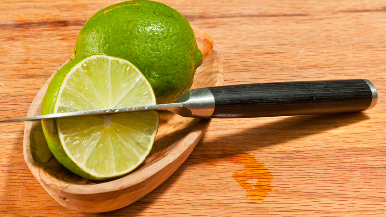 Two limes on a wooden plate with a paring knife cut into one of them