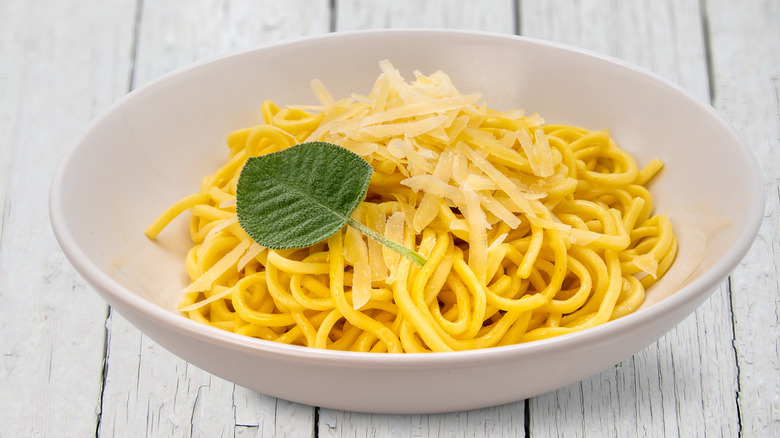Tagliolini spaghetti egg pasta with butter and sage sauce with parmesan flakes in white dish on white wooden table