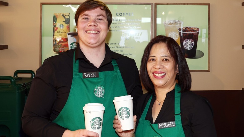 Male and female baristas pose with Starbucks drinks.