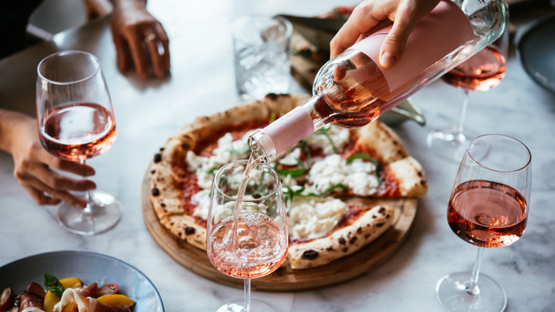 hand pouring a glass of rosé in front of a pizza