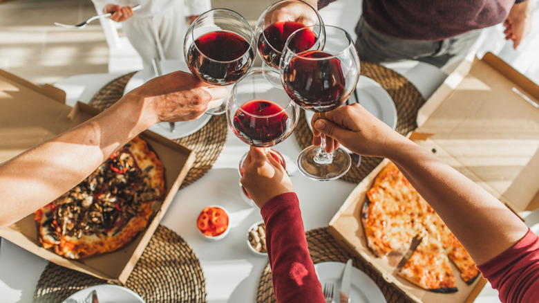 Hands holding wine glasses above pizza boxes