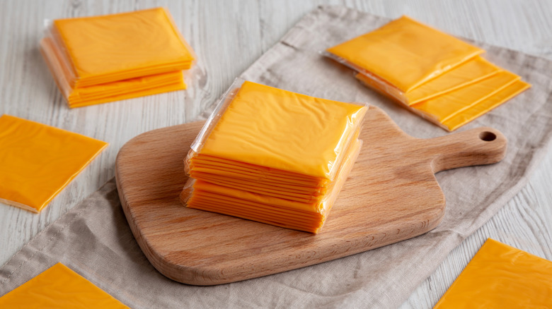 Stacks of cheese scattered on top of a table with a chopping board and towel.