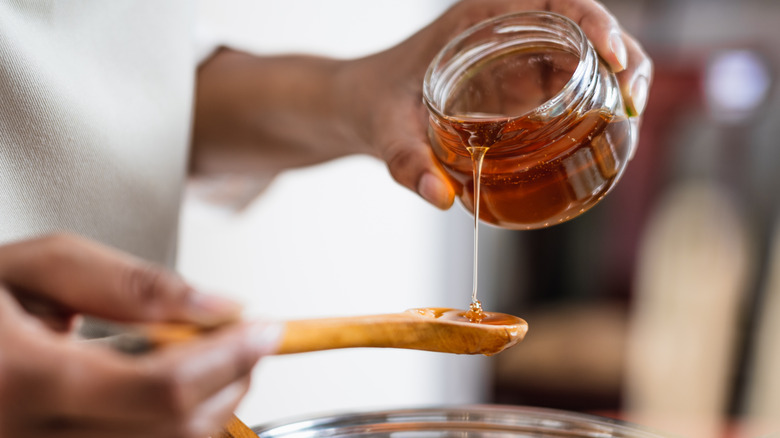 A home cook pours golden syrup from a jar into a wooden spoon