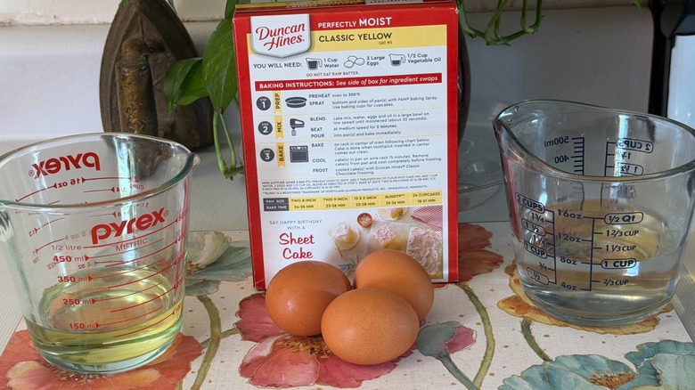 The back of the Duncan Hines cake mix box next to three eggs and measuring cups of oil and water.