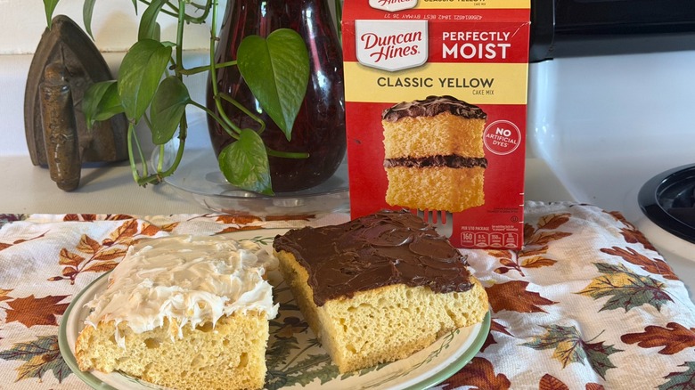 Two pieces of Duncan Hines yellow cake, one with chocolate frosting and one with cream cheese frosting, on a plate in front of the box.